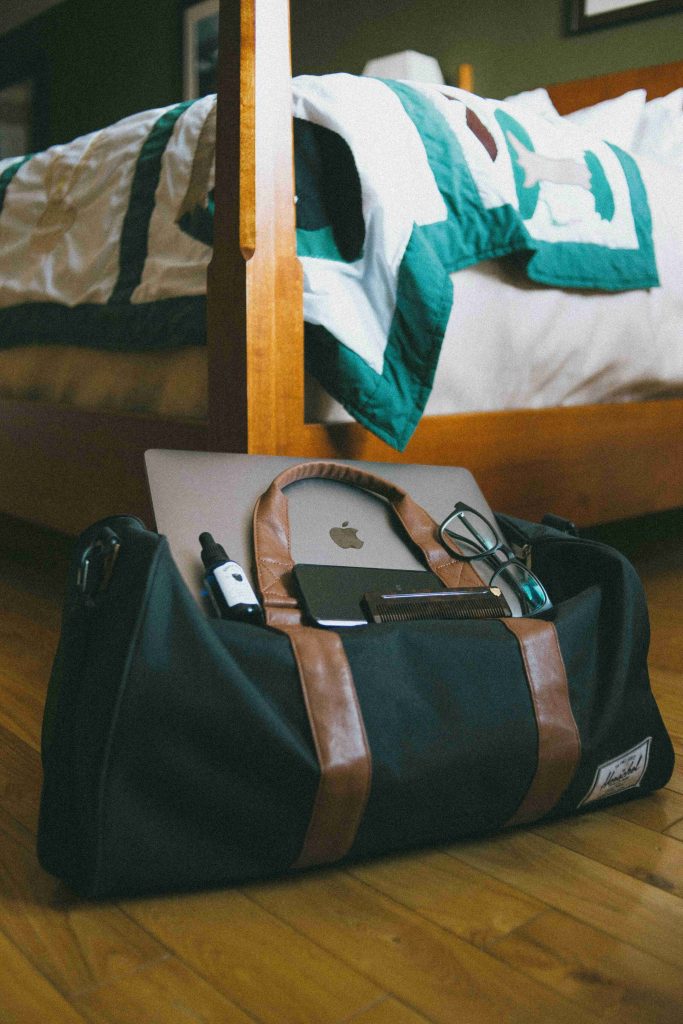 A duffel bag on a wooden floor next toa bed, partially packed with live-in care essentials, including a laptop, glasses, notebook - suggesting preparation for live-in placement.