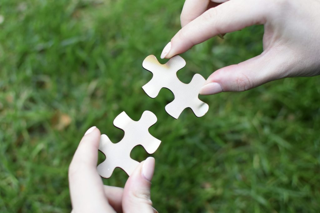 Two hands holding puzzle pieces, carefully aligning them together—symbolising how patience is needed to make things fit in care and in life.