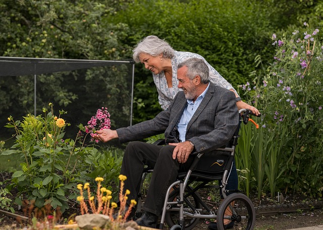 An elderly couple enjoying a garden together, with one partner in a wheelchair and the other offering gentle support — a warm moment reflecting person-centred care, dignity, and shared connection in everyday life.