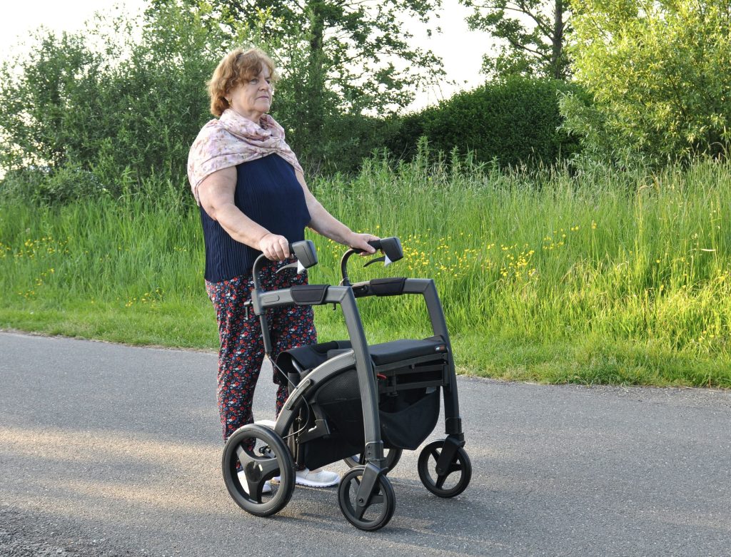 A woman with a four-wheel walker walking on the road, representing an independent living aid.